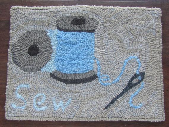 hooked rug with spools of thread and a needle