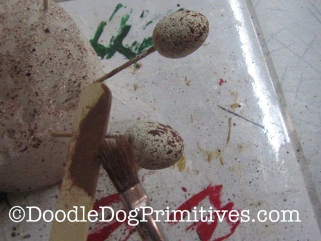 Using the paint brush and popsicle stick to splatter the styrofoam eggs with paint